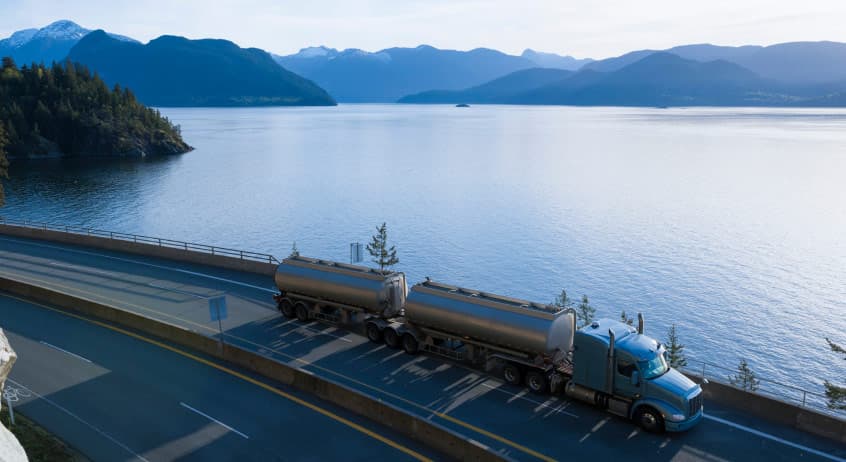 tanker trailers loaded with biofuel being transported by a lake in a pristine, forested area